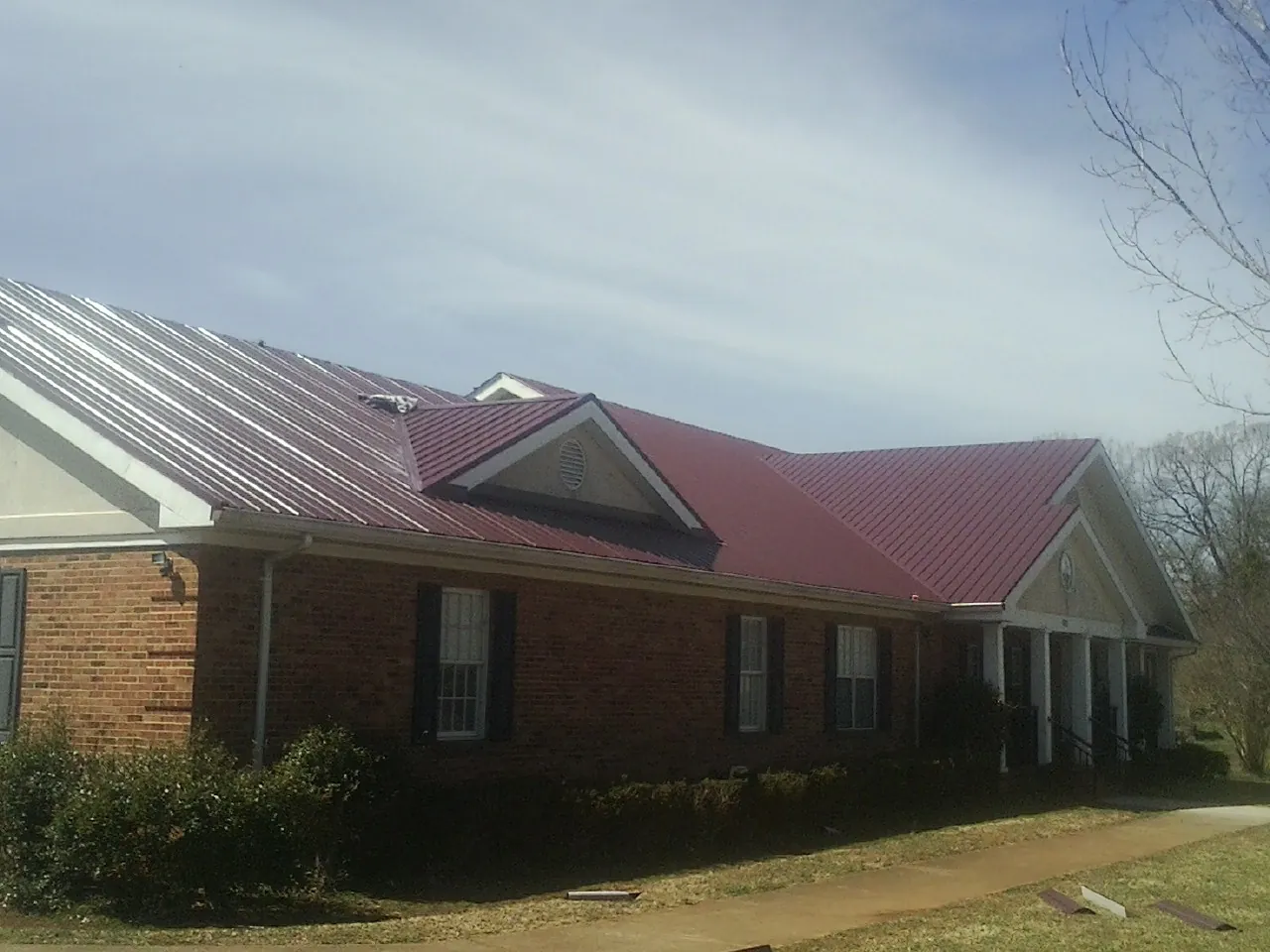 Red metal roof with gabled entries on a long brick building, from a Hail Damage Roof Repair job in Lawton
