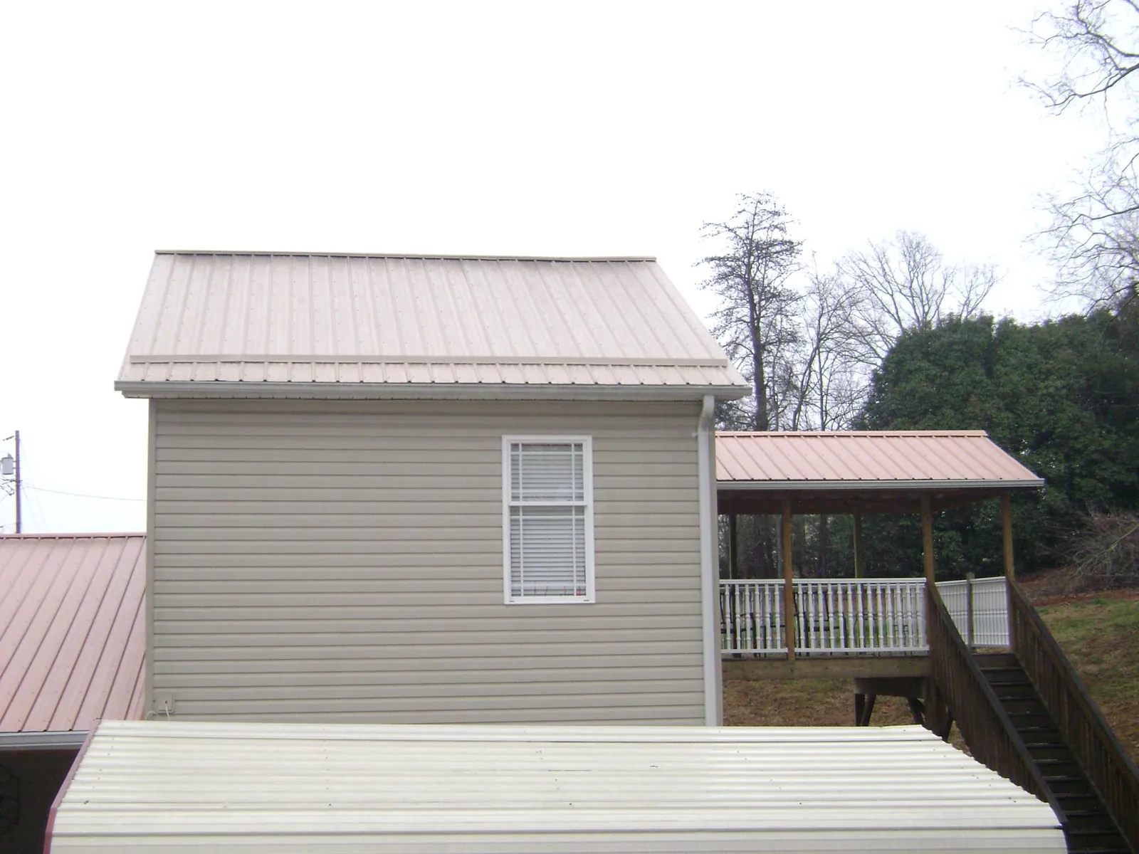 Tan metal roofs on a two story addition and attached porch, from a Roof Replacement job in Lawton